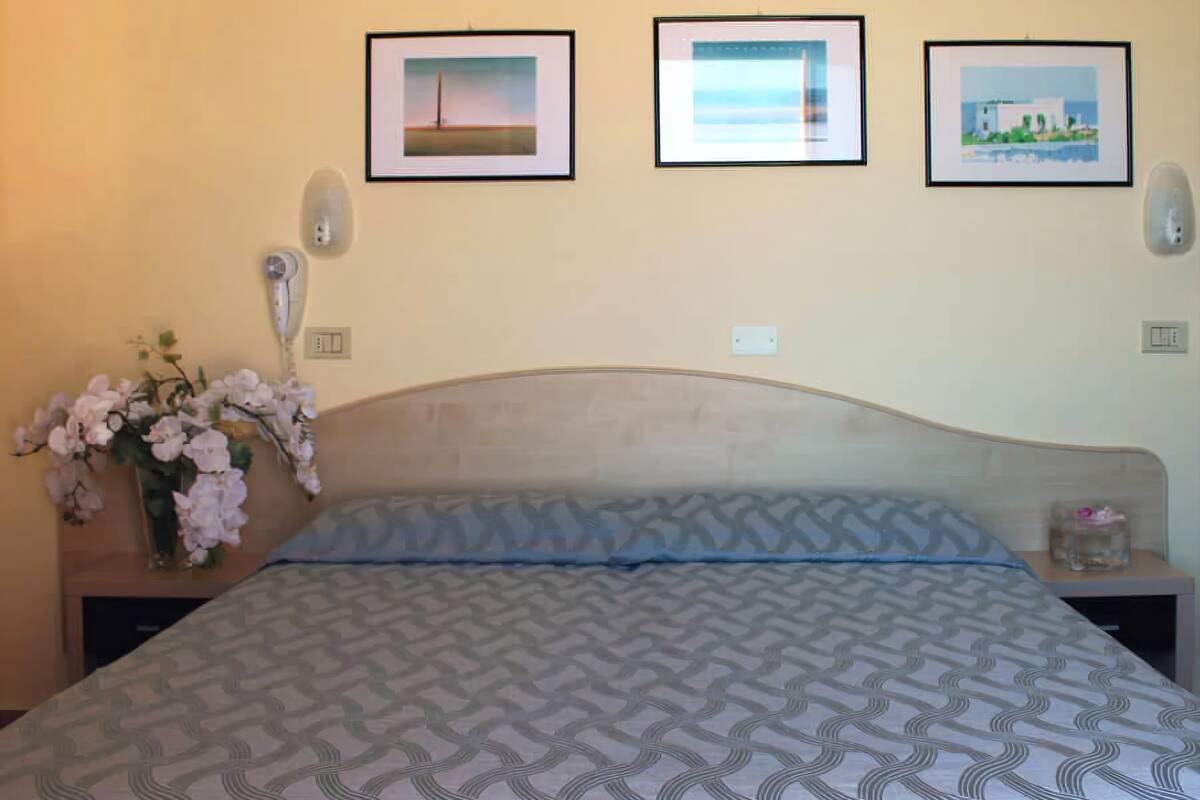 A hotel room with a bed, a nightstand with a vase of flowers, and three framed pictures on the wall.