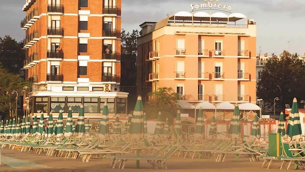 Un hotel con varios pisos, asientos exteriores con sombrillas y un letrero que indica el nombre 'Sombrero'.