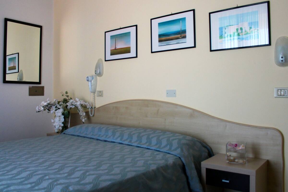 A hotel room with a bed, a nightstand, a mirror, and three framed pictures on the wall.