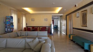Vestíbulo de hotel con un amplio sofá seccional color beige, un mostrador de recepción y un pasillo que conduce a un comedor.
