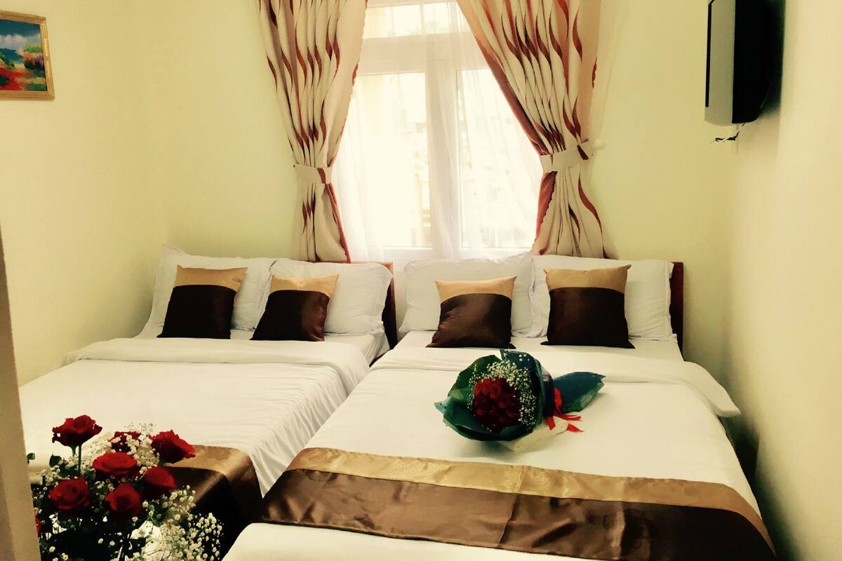 A hotel room with two beds, a bouquet of red roses, and a painting on the wall.