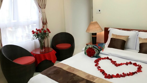 A hotel room with a bed, two armchairs, a small table with a vase of flowers, a lamp, and a bouquet of red roses. - Full Moon Da Lat Hotel (Cam Ly - Da Lat)