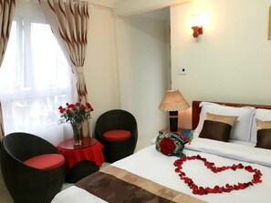 A hotel room with a bed, two armchairs, a small table with a vase of flowers, a lamp, and a bouquet of red roses. - Full Moon Da Lat Hotel (Cam Ly - Da Lat)