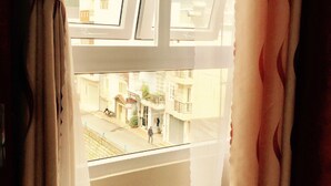 A window with white curtains, a view of a street with buildings and a person walking. - Full Moon Da Lat Hotel (Cam Ly - Da Lat)