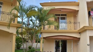 A two-story building with a balcony, a door with a glass panel, and a small garden area with palm trees and shrubs. - Residence Mon Choisy (Mont Choisy)