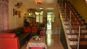 A living room with a red sofa, a coffee table with a floral tablecloth, and a staircase with a red handrail. - Residence Mon Choisy (Mont Choisy)