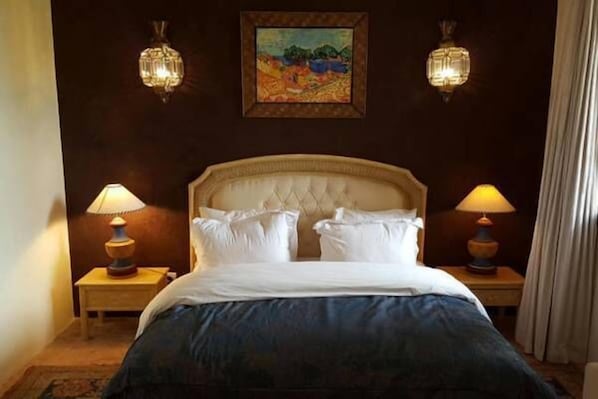 A hotel room with a large bed, two bedside lamps, a painting on the wall, and a curtain on the window.