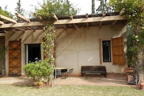A rustic outdoor seating area with a wooden pergola, a bench, and a table with chairs.