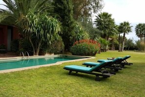 A pool area with a clear pool, green lawn, and lounge chairs.