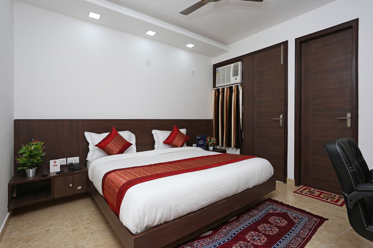 A modern hotel room with a large bed, a nightstand, a desk, a chair, and a wardrobe.