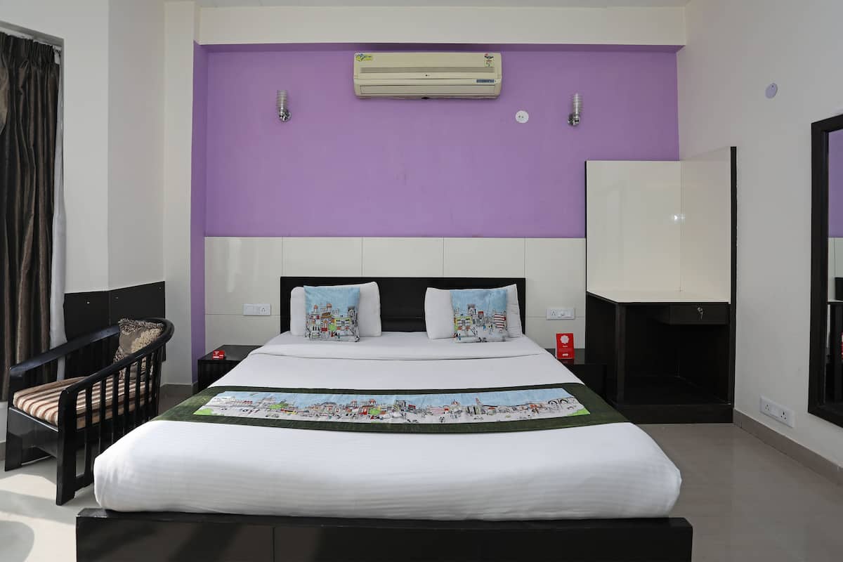 A hotel room with a large bed, a headboard, a nightstand, a chair, an air conditioner, and a mirror.