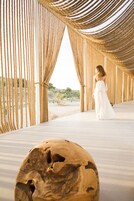 Una estructura de madera con un cortinero de cuerda, un banco de madera y una persona vestida de blanco.