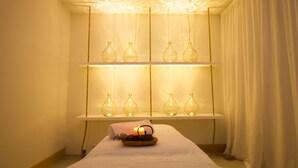 A spa room with a massage table, candles, and glass bottles on shelves. - Aelia Wellness Retreat (Analiontas)