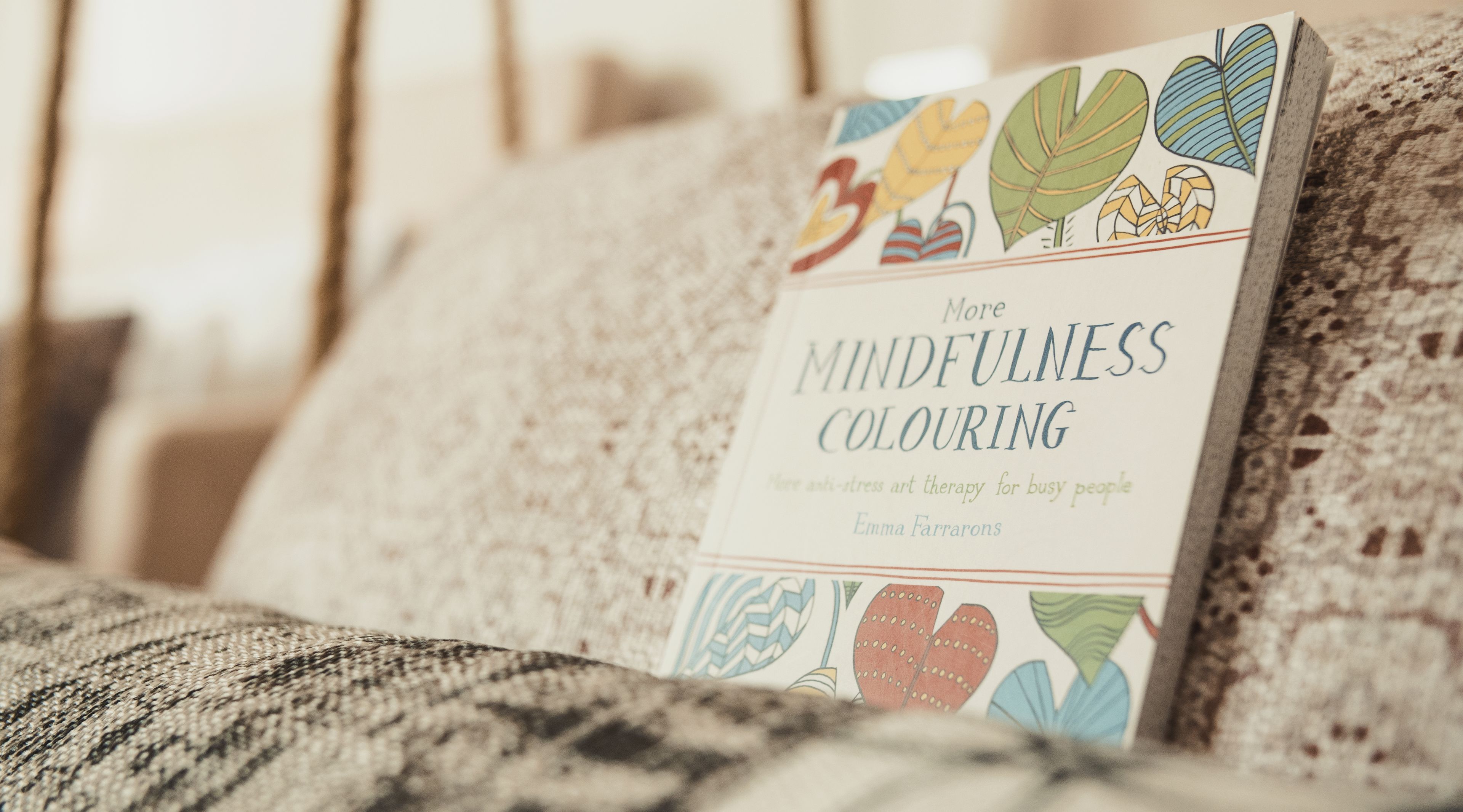 A book titled 'More Mindfulness Colouring' on a textured sofa.