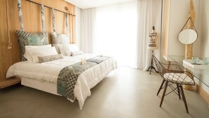 A bedroom with a wooden headboard, a bed with white bedding, a glass table with a chair, and a large window with curtains. - Aelia Wellness Retreat (Analiontas)