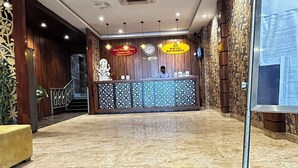 Zona de recepción de hotel con suelo de mármol, mostrador de recepción y un tablón informativo en la pared.