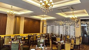 Un restaurante con piso de madera, sillas tapizadas en verde y candelabros. Las mesas están dispuestas con manteles blancos y centros de mesa.