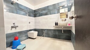 A bathroom with a white sink, a mirror, and a shower. There is a toilet and a small blue stool.