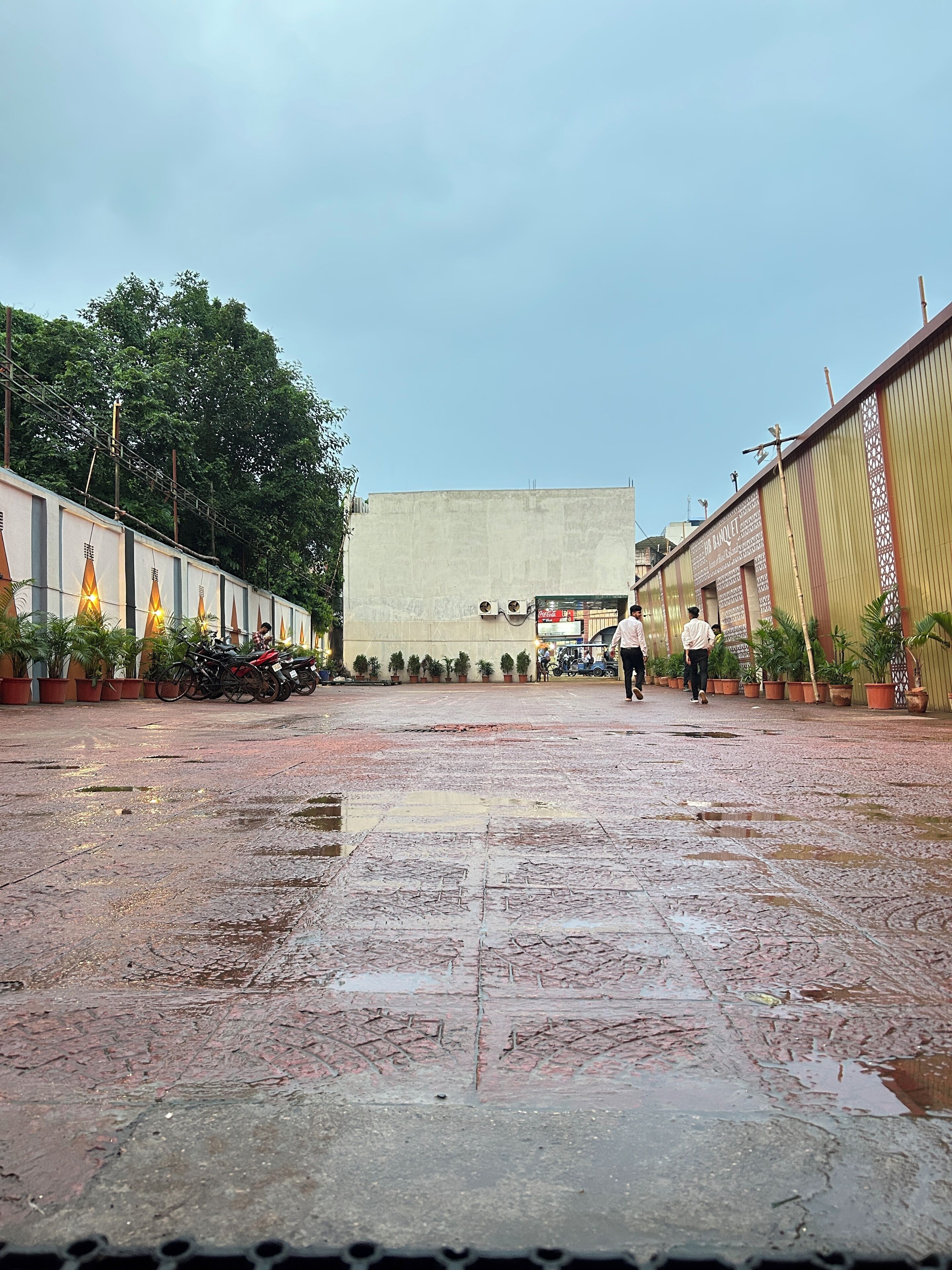 A courtyard with a wet ground, potted plants, and a building with a sign reading "FOOD HANLET".