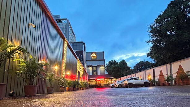 Un patio empedrado con plantas en macetas, un edificio con señalización iluminada y un vehículo estacionado.