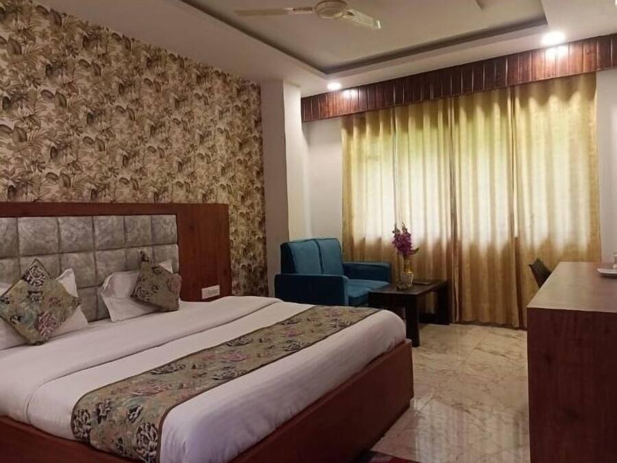 A hotel room with a large bed, a blue armchair, a small table with a vase, and a curtain.