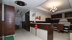 Uma área de recepção de hotel com um balcão de madeira, um ventilador, um candelabro e uma placa indicando a marca OYO.