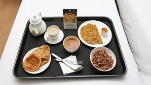 Uma bandeja com um bule, xícaras, um prato de pães achatados, uma tigela de sopa, um prato com um pão achatado dobrado, um pote de amendoins e um cardápio.