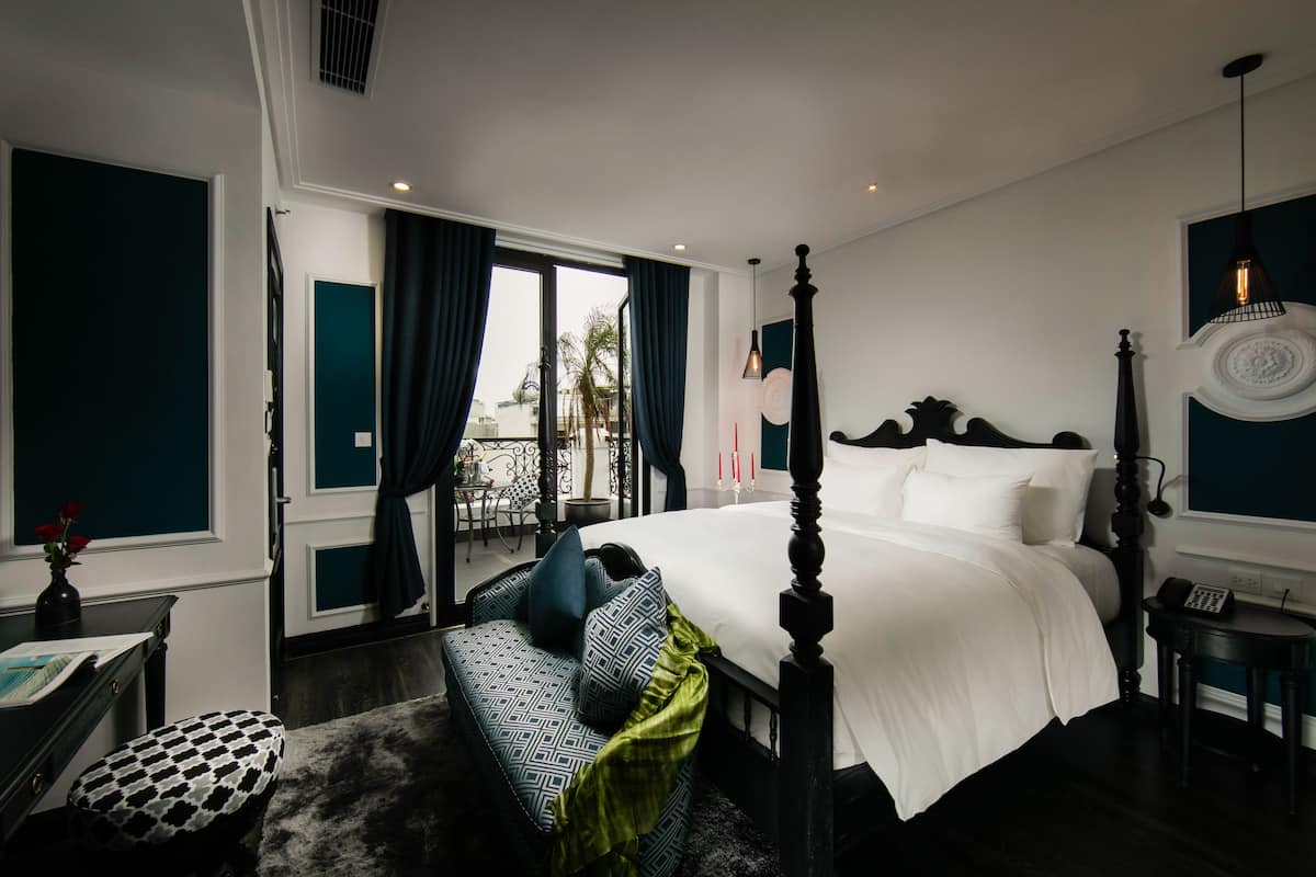 A bedroom with a four-poster bed, a sofa, a small table, and a view of the outdoors.
