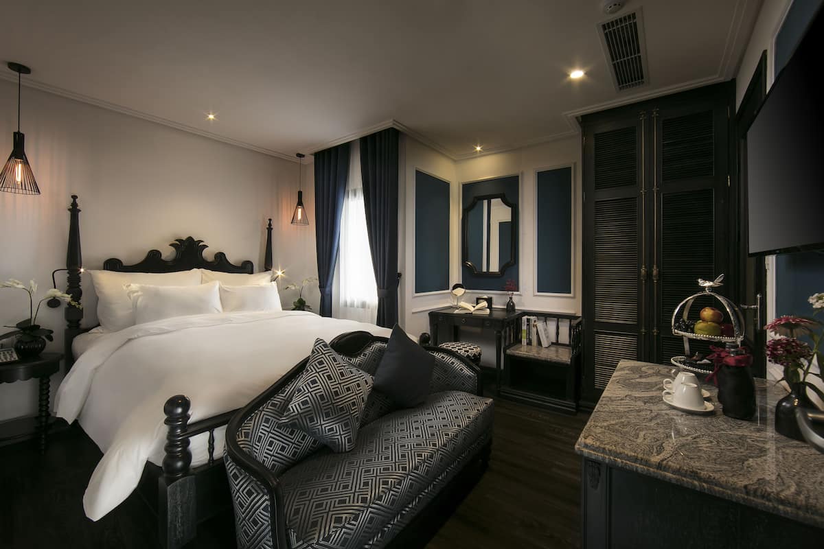 A bedroom with a large bed, a bedside table, a dresser, and a vanity with a mirror.
