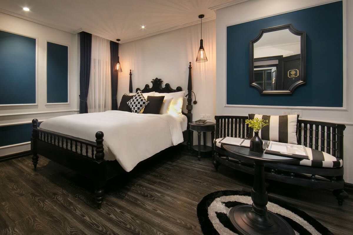 A bedroom with a large bed, a bedside table, a chair, a mirror, and a window.
