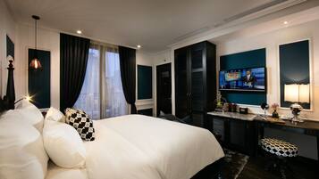 A hotel room with a large bed, a desk with a television, and a view of the city through the window.