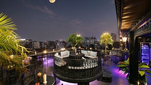 Un bar en la azotea con una zona de estar circular, rodeado de palmeras y vistas de la ciudad.