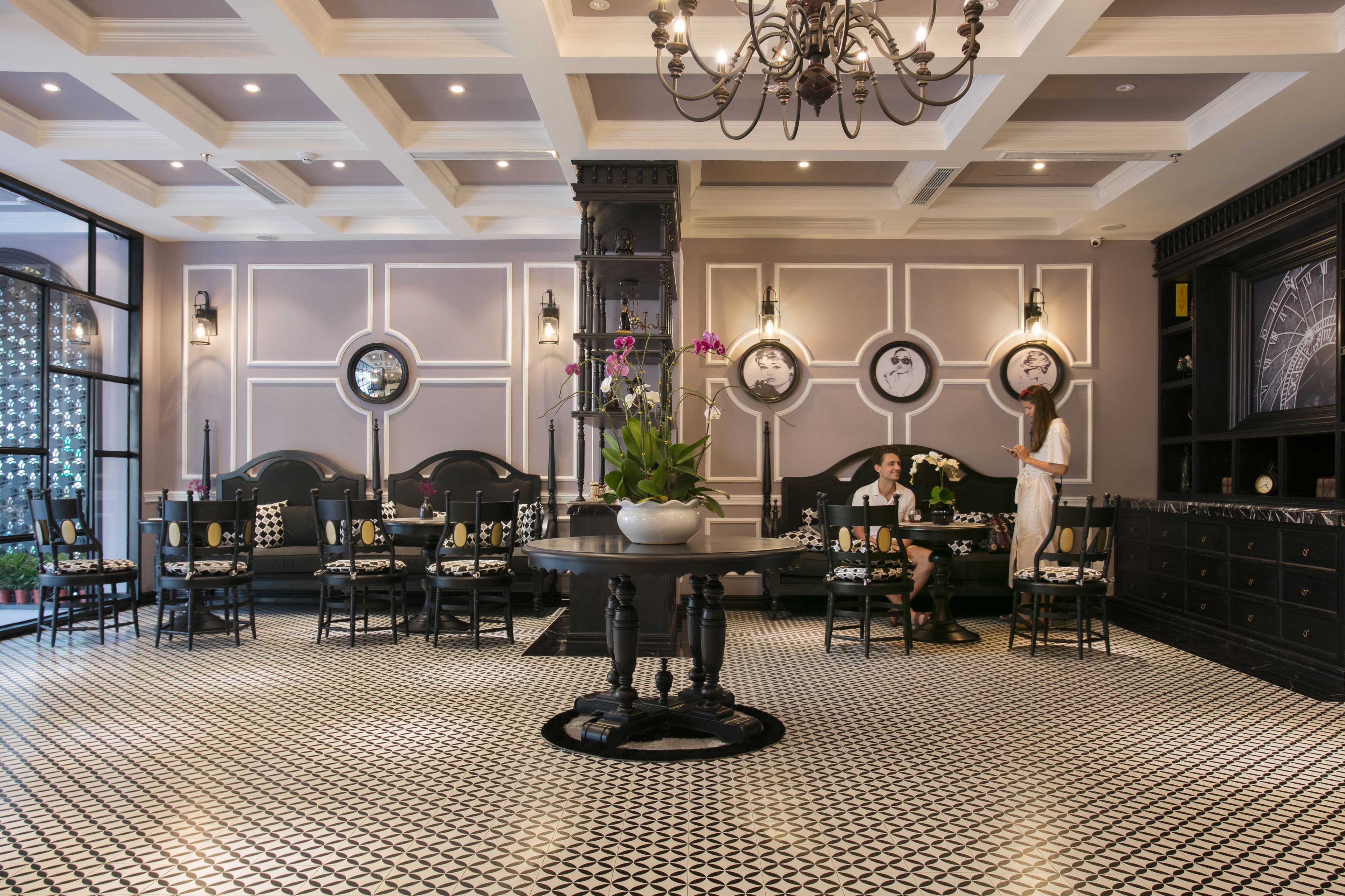 A hotel lobby with a checkered floor, a central round table, and a chandelier.