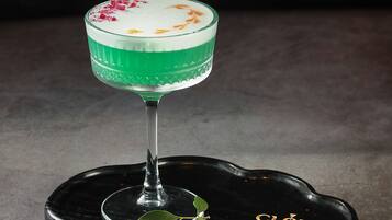 A cocktail glass with a green liquid and a white foam top, placed on a black tray with a leaf and the text "CLOUD SKY BAR".