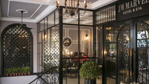 Entrada de un hotel con una reja de hierro forjado, un candelabro y un letrero que dice "JM Marvel Hotel & Spa".