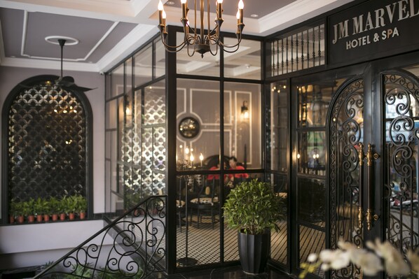 Entrada de un hotel con una reja de hierro forjado, un candelabro y un letrero que dice "JM Marvel Hotel & Spa".