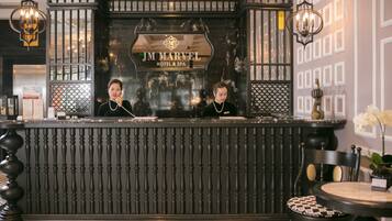 A reception desk at JM Marvel Hotel & Spa with a marble backdrop and two receptionists.