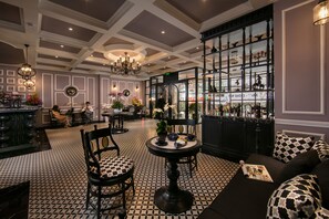 A bar area with a black and white checkered floor, a round table with a vase of flowers, and a sofa with patterned cushions. - JM Marvel Hotel & Spa (Hanoi)