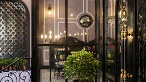 Entrada de un hotel con una reja de hierro negro, una planta en maceta y un candelabro.
