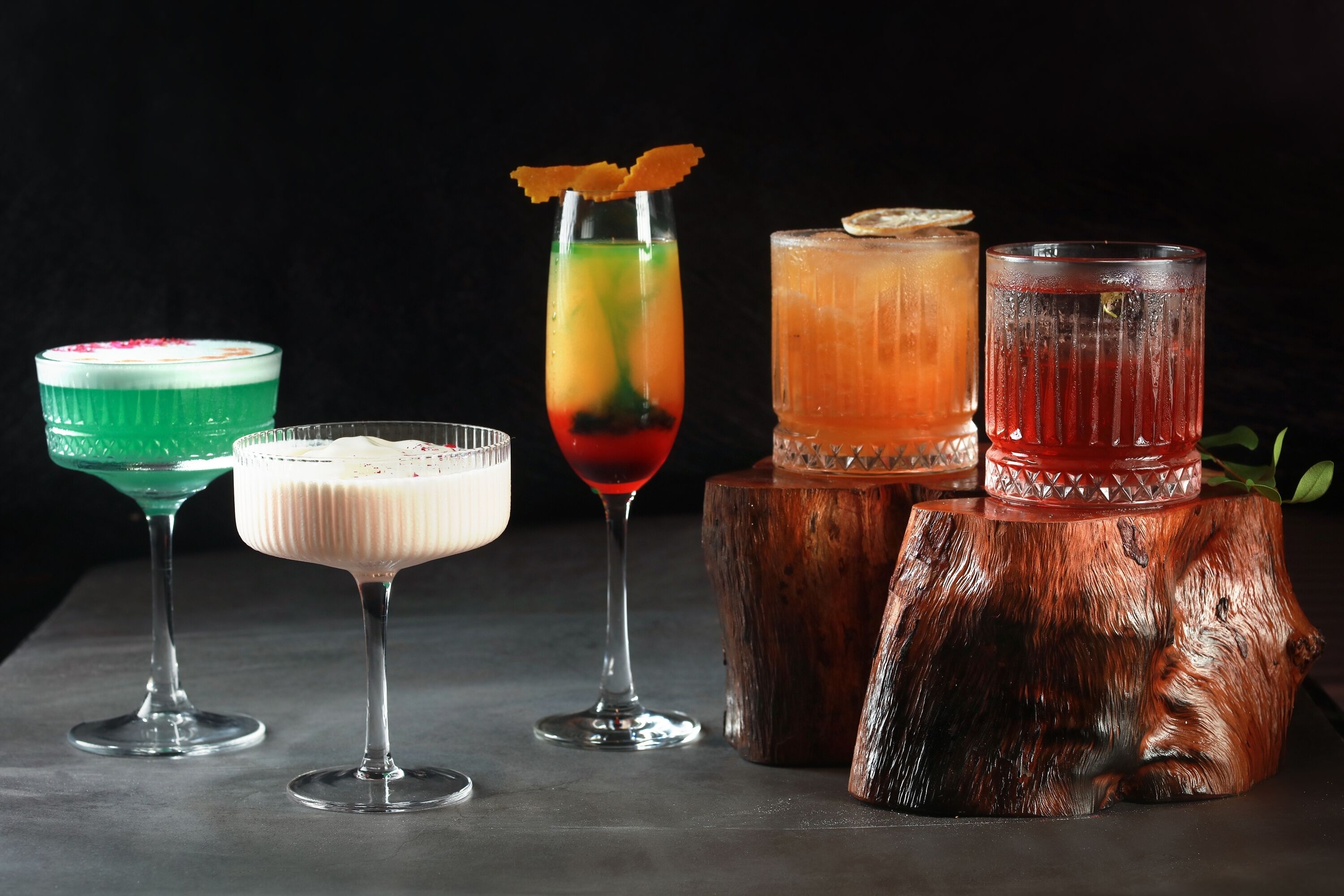 Vier Cocktails in verschiedenen Gläsern auf einer Holztischplatte.