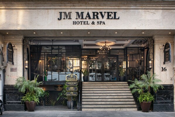 La entrada al Hotel JM Marvel & Spa, con un acceso imponente que incluye escalones, una araña y plantas en macetas.