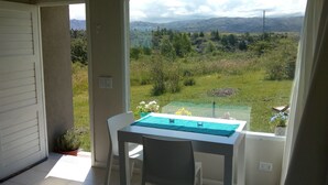 A balcony with a table and chairs, overlooking a green landscape with mountains in the distance. - Bernalina (La Cumbrecita)