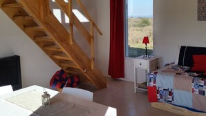 A bedroom with a wooden staircase, a window with a view of the outdoors, a bedside table with a lamp, and a bed with a patterned blanket. - Bernalina (La Cumbrecita)