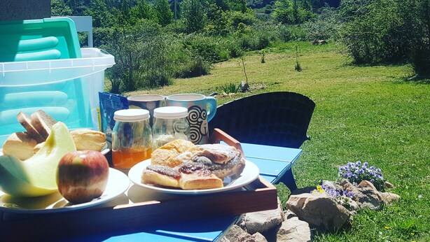 A table with food and drinks, a chair, and a view of a green landscape with hills in the background. - Bernalina (La Cumbrecita)