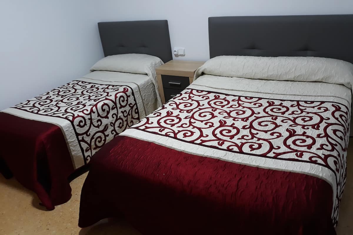 Dos camas individuales con cabeceras, una mesita de noche y un enchufe en la pared.