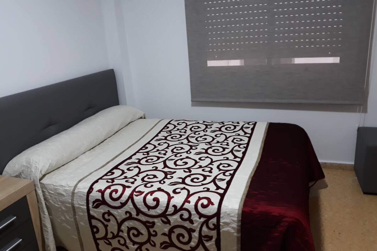 Un dormitorio con cama, cómoda, ventana con persianas y alfombra roja.