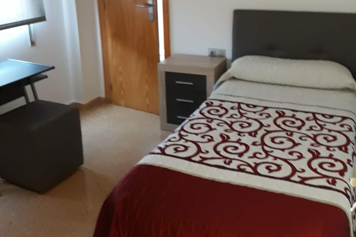 Un dormitorio con cama, escritorio, armario y unidad de aire acondicionado.