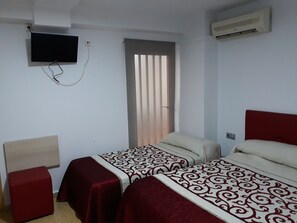Een hotelkamer met twee bedden, een aan de muur bevestigde televisie, een airconditioner en een raam met jaloezieën.