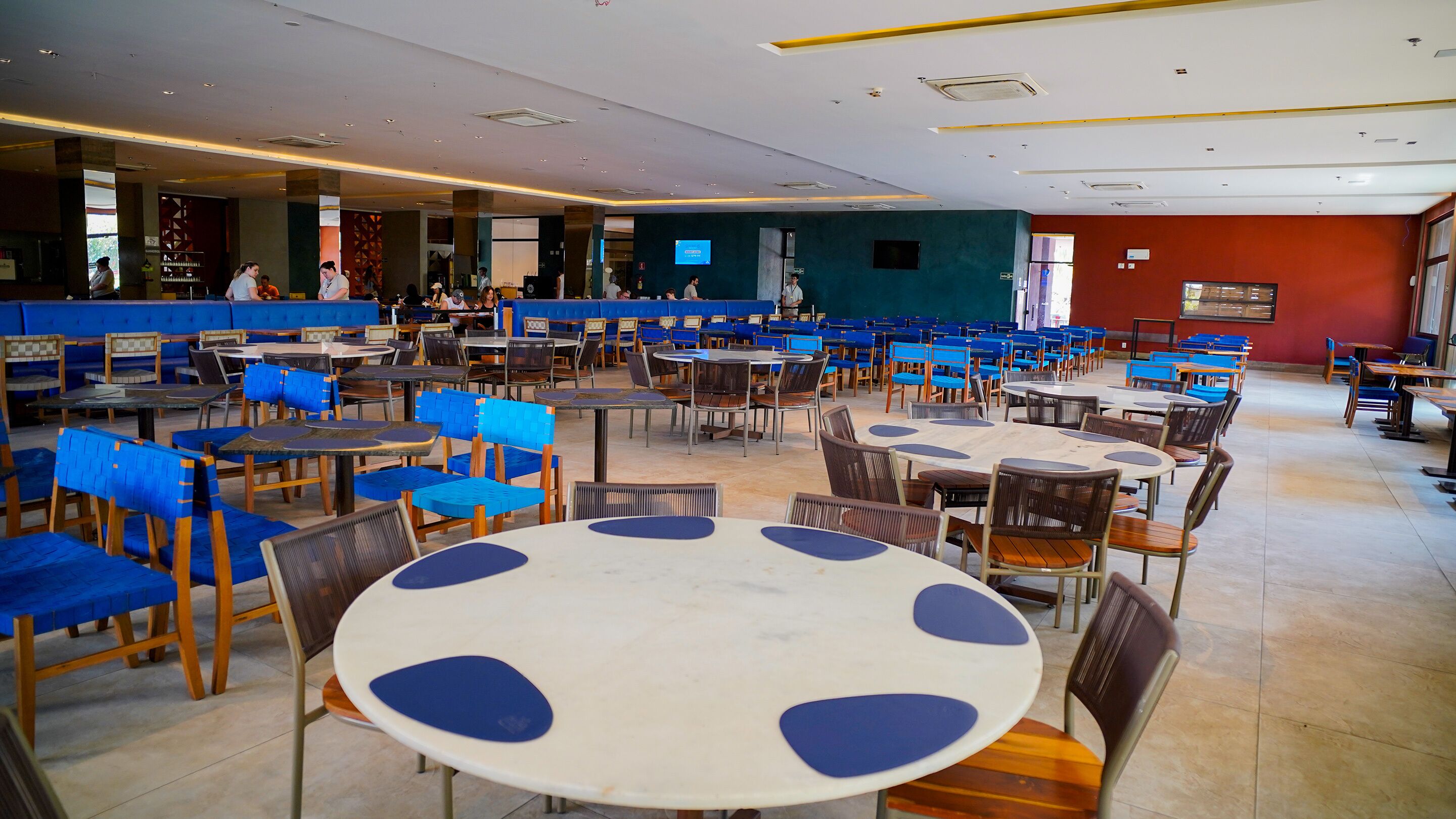 A spacious indoor dining area with multiple tables and chairs, a counter with a digital screen, and a view of the outside through a large window.