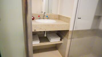 A bathroom with a white sink, two faucets, a mirror, and a towel shelf.